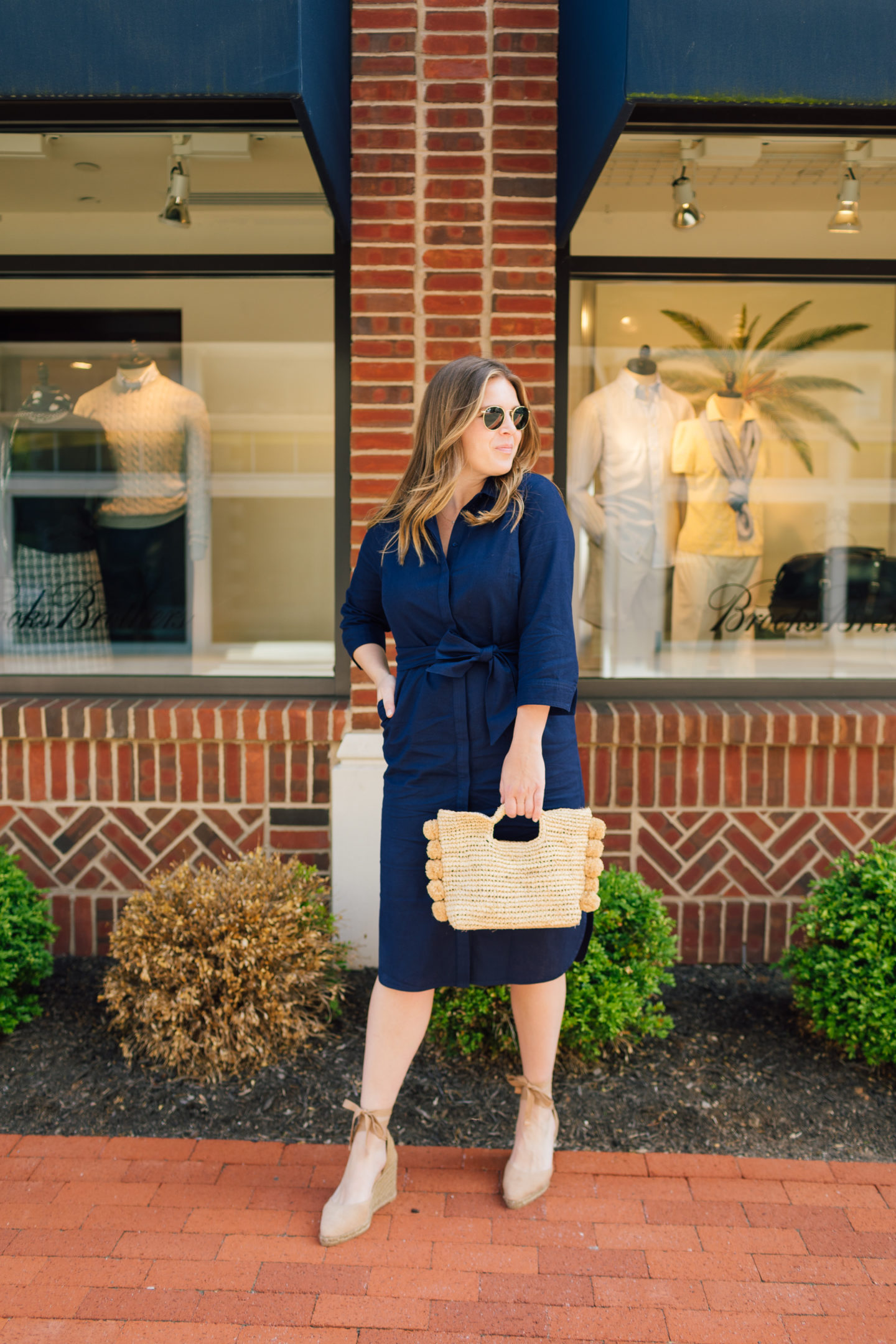 Emily Lucille wearing the Boden Linen Shirt Dress in Navy with a Hat Attack Straw Bag and Castaner Wedges